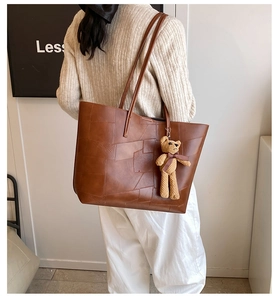 Dettaglio di una grande borsa tote marrone vintage con cuciture e un ciondolo a orsetto