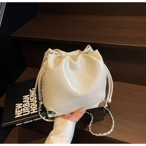 Detail of cream drawstring bucket bag with silver metal corners and chain strap
