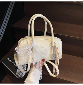 Detailed view of cream leather Boston bag with lace bow and tennis racket charm accessory
