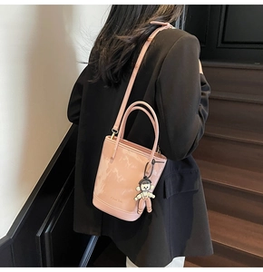 Vue détaillée du sac seau en cuir verni rose avec poignée et breloque mignonne sur la bandoulière