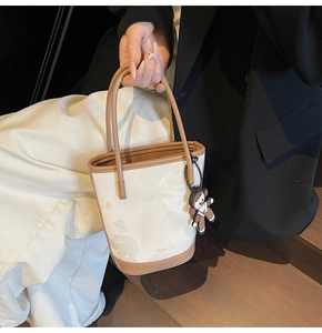 Détail du sac seau bicolore crème et marron avec breloque ours et logo de la marque