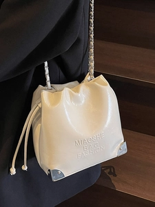 Creamy white drawstring bucket bag with silver chain strap shown on model over dark stairs