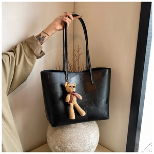 Dettaglio di borsa tote in pelle nera patchwork con ciondolo a orsetto e doppie tracolle