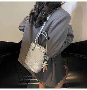 Sac seau argenté métallisé avec bijou de sac porté en bandoulière sur une veste grise