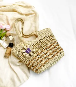 Detail view of woven straw beach bag featuring large flower pendant and butterfly motif