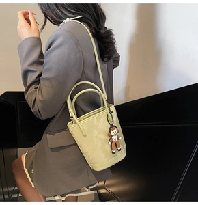 Détail d'un sac seau en similicuir vert pâle mat avec breloque poupée et bandoulière