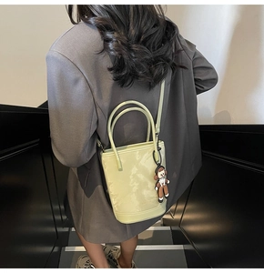 Détail du sac seau vert clair avec un charm de poupée et une bandoulière réglable
