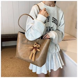 Dettaglio di una borsa tote grande in pelle marrone con trama patchwork e ciondolo orso