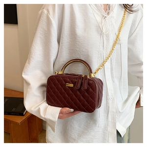 Detail of burgundy quilted leather handbag with gold metal handle and chain strap on model