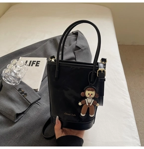 Détail du sac seau en cuir noir avec logo doré et breloque poupée de dessin animé