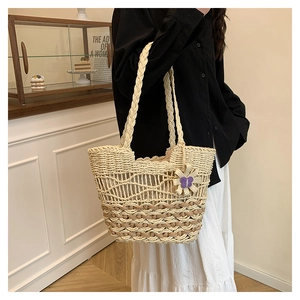 Close-up of beige woven straw tote bag with brown trim and purple floral pendant charm