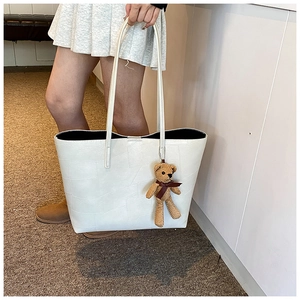 Dettaglio della borsa tote bianca con texture geometrica e ciondolo orsetto