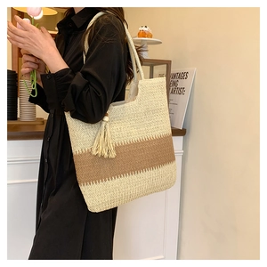 Detail view of woven straw tote bag featuring beige brown stripes and fringe tassel