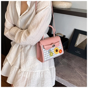 Detail of pink PU leather handbag with floral accents and plaid pattern on white dress