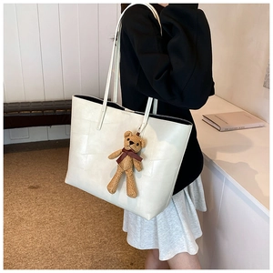 Dettaglio della borsa tote off-white con trama geometrica e ciondolo orsetto marrone