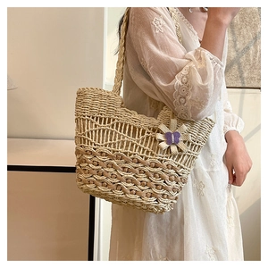 Detailed close-up of straw woven tote bag featuring a purple butterfly floral charm