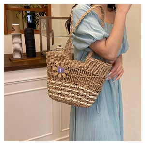 Detail of woven straw tote bag with sunflower pendant and striped mesh pattern on a strap