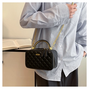 Detail of classic black quilted box bag with gold metal handle and dual zipper closure