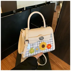 Close-up of cream square bag featuring grid pattern, floral appliques and silver rotary lock