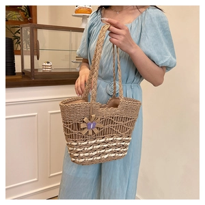 Detail of hand-woven straw tote bag with white stripes and floral pendant decoration