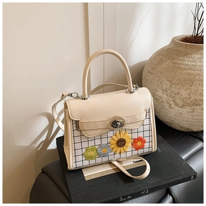 Detail view of cream crossbody bag with floral patches and checkered pattern on a book