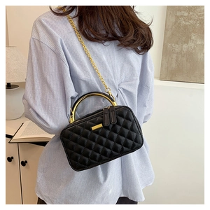 Rear view of model wearing a black quilted leather box bag with gold metal handle