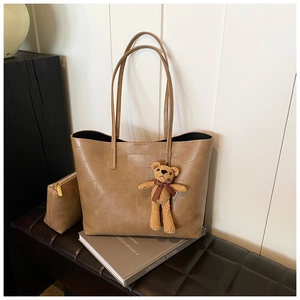 Dettaglio della borsa tote in pelle kaki con texture patchwork e un piccolo ciondolo a orsetto