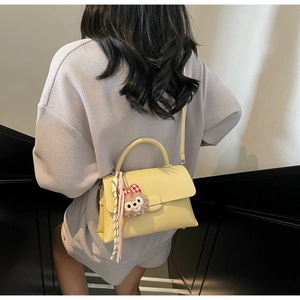 Détail du sac bandoulière en cuir jaune avec breloque ours en peluche et ruban rayé