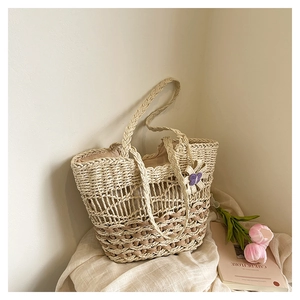 Detail of handmade straw tote bag featuring hollow mesh weave and decorative floral charm