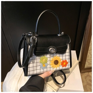 Detail view of the black and white plaid handbag with three colorful woven floral patches
