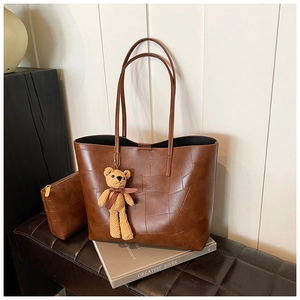 Dettaglio di un set tote in ecopelle marrone con trama patchwork e ciondolo a orsetto