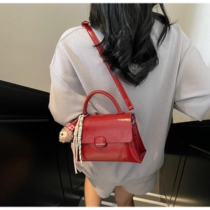 Détail du sac à main rouge en cuir verni brillant avec bandoulière et breloque ours