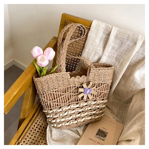 Detail of a woven straw tote bag with floral charm on a vintage chair for beach vacation