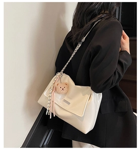 White glossy tote bag with chain strap and teddy bear charm shown on black blazer