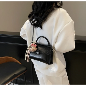 Détail du sac à main en cuir verni noir avec fermoir argenté et charm en peluche doux