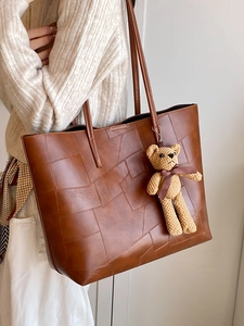 Borsa tote in pelle marrone con ciondolo a orsetto indossata da una modella casual