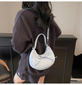 Détail du sac demi-lune bleu clair avec nœud porté par un mannequin en sweat à capuche gris