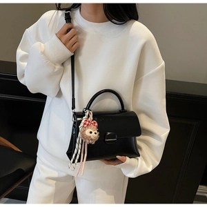Détail du petit sac carré noir avec une breloque en peluche et un fermoir métallique chic