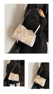 Detail of white glossy leather tote bag featuring a metal logo and plush bear charm