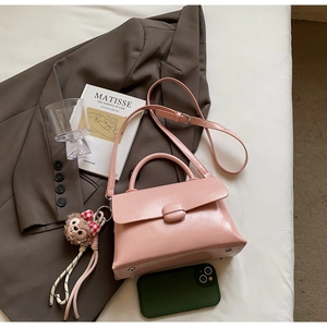 Détail d'un sac à bandoulière rose avec rabat arrondi et breloque ours en peluche