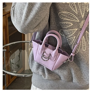 Dettaglio mini borsa viola in pelle martellata con anelli metallici e logo su maglia grigia