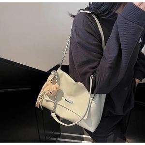 Detail view of cream leather tote bag featuring metal chain strap and plush bear charm
