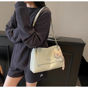 Detail view of cream-white patent leather shoulder bag with plush bear charm and tassels