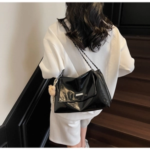 Detail view of black glossy shoulder bag featuring silver chain strap and plush bear charm