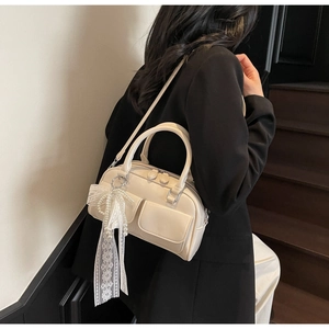 Detail view of cream Boston bag featuring front flap pockets and lace bow charm