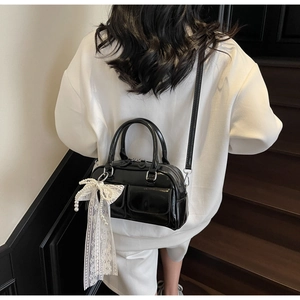 Detail view of black patent leather Boston bag with lace bow and pearl charm accents