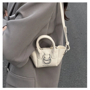 Dettaglio mini borsa a tracolla in pelle crema con doppi anelli metallici e texture