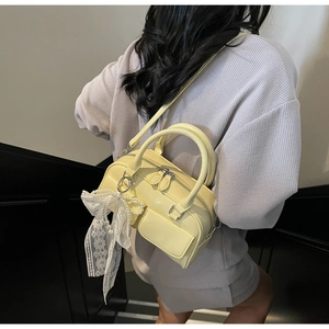 Detailed view of cream Boston bag featuring delicate lace bow and pearl charm accessories