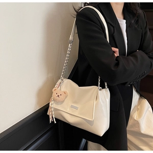 Detail of cream patent leather tote bag with silver chain strap and bear charm accessory