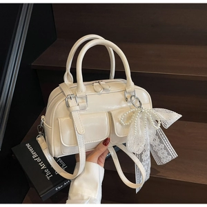Detail view of cream Boston bag with pearl bow charm and glossy synthetic leather finish